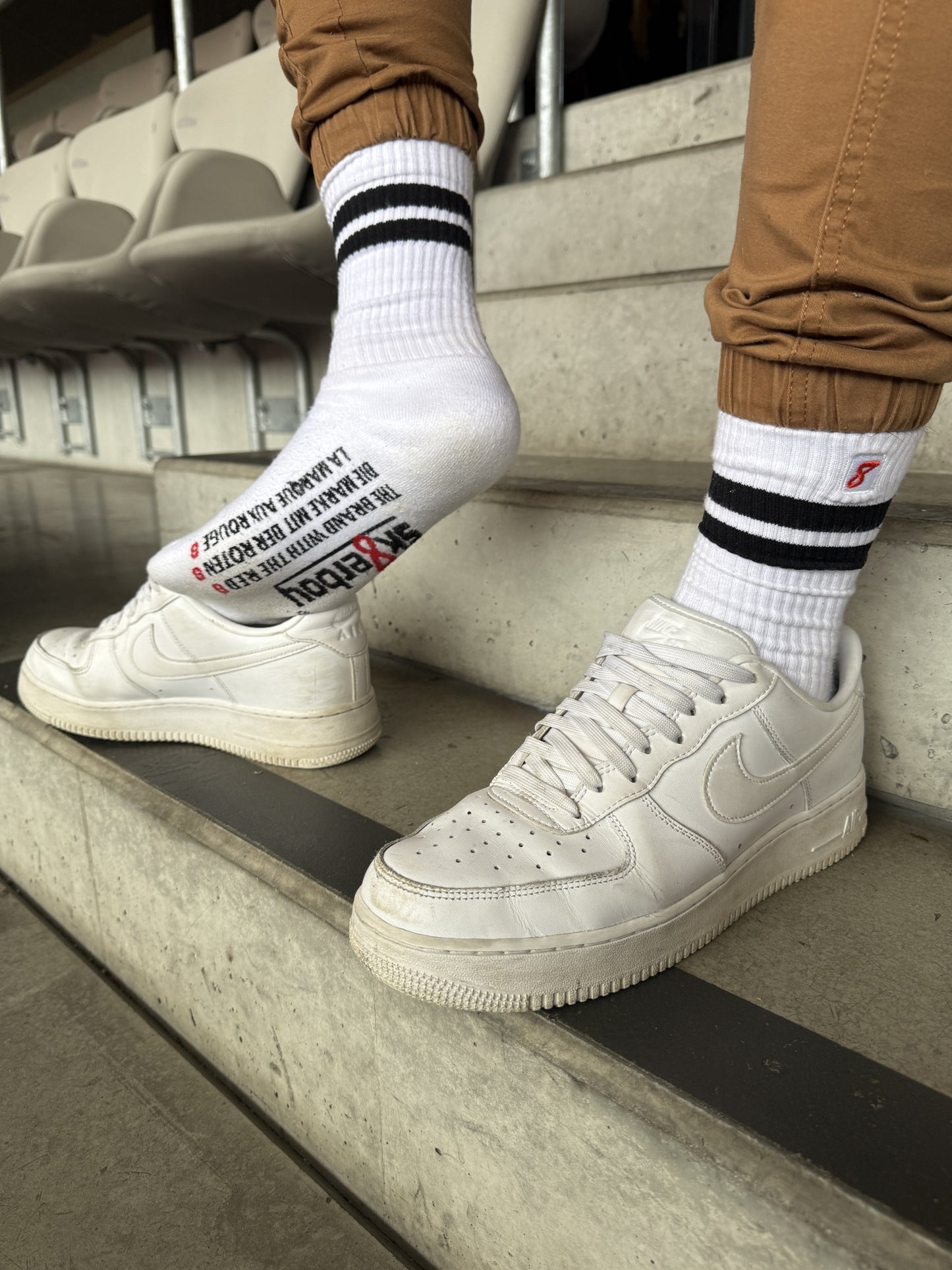 Lässiger Stadion-Moment: Sk8erboy® Retro Socken mit schwarzen Streifen und auffälligem Print auf der Sohle, kombiniert mit weißen Nike Air Force 1 – stylischer Streetwear-Look mit Attitude.
