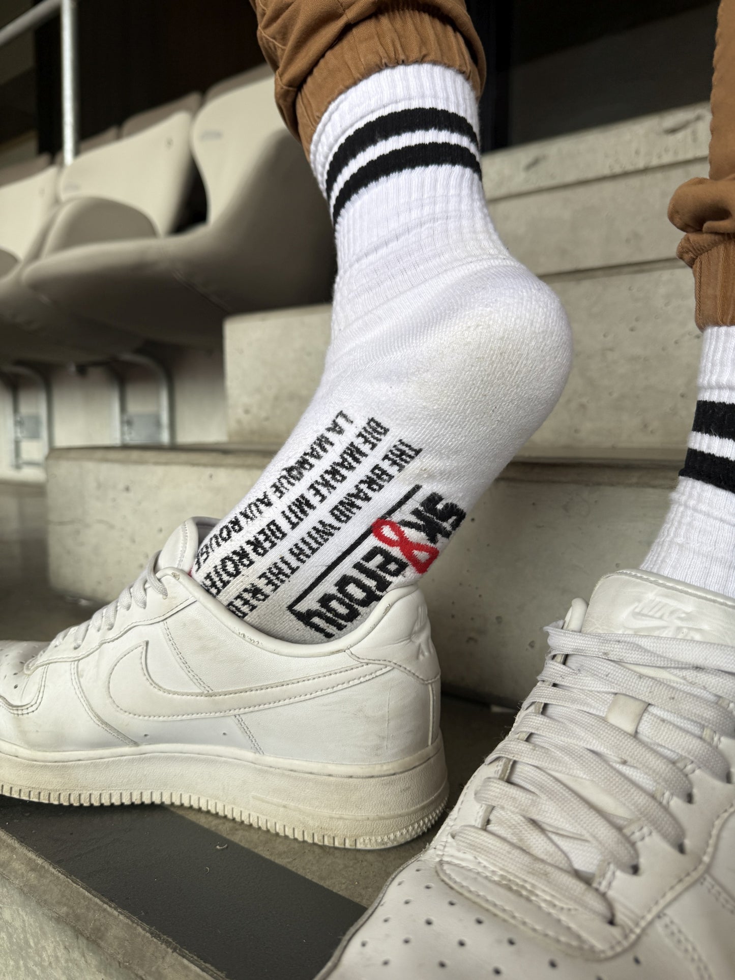 Lässiger Stadion-Moment: Sk8erboy® Retro Socken mit schwarzen Streifen und auffälligem Print auf der Sohle, kombiniert mit weißen Nike Air Force 1 – stylischer Streetwear-Look mit Attitude.