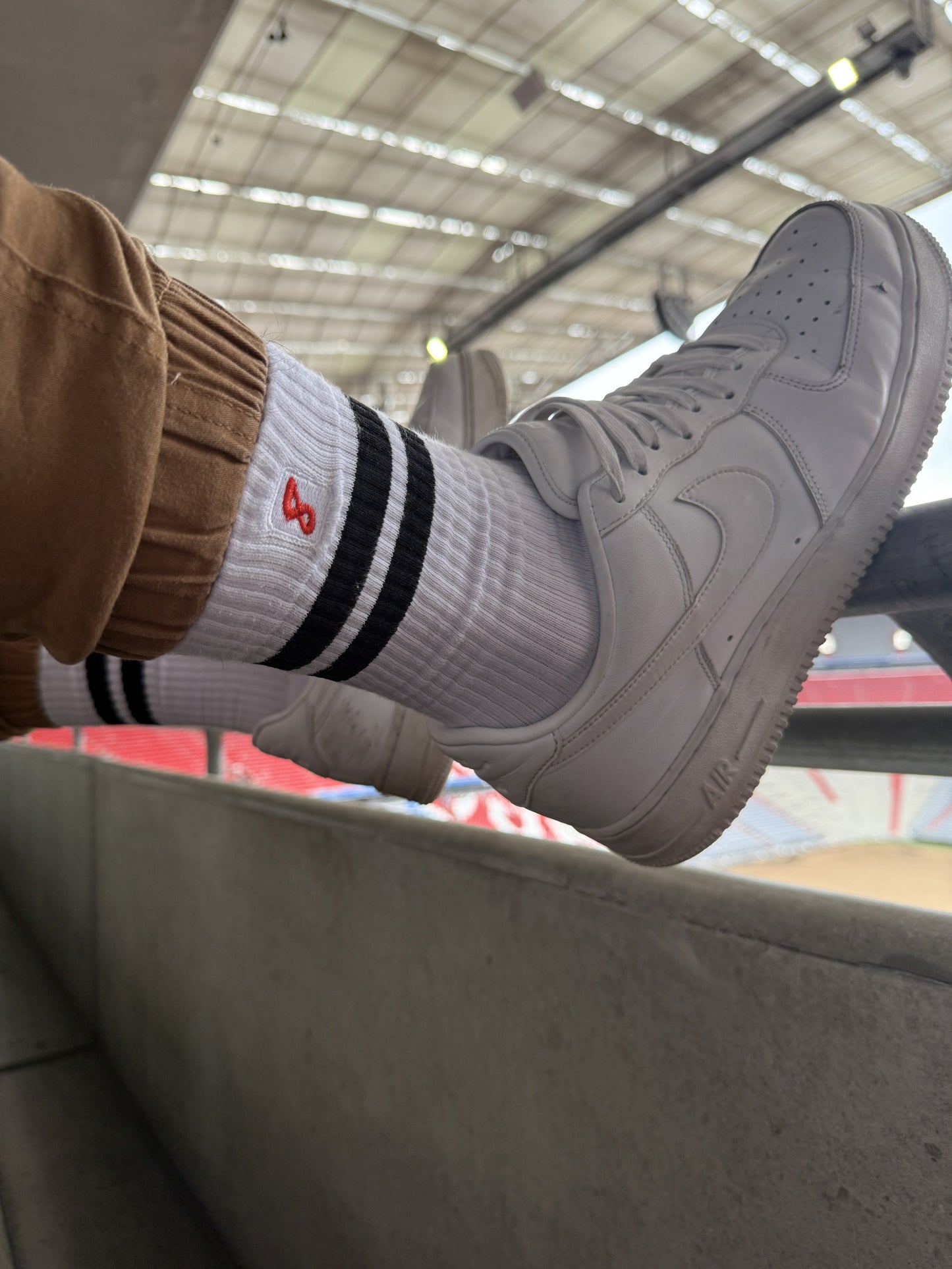Nahaufnahme von Sk8erboy® Retro Socken mit schwarzen Streifen, getragen mit weißen Nike-Sneakern im Stadion – sportlicher Gay-Look mit Statement-Faktor.