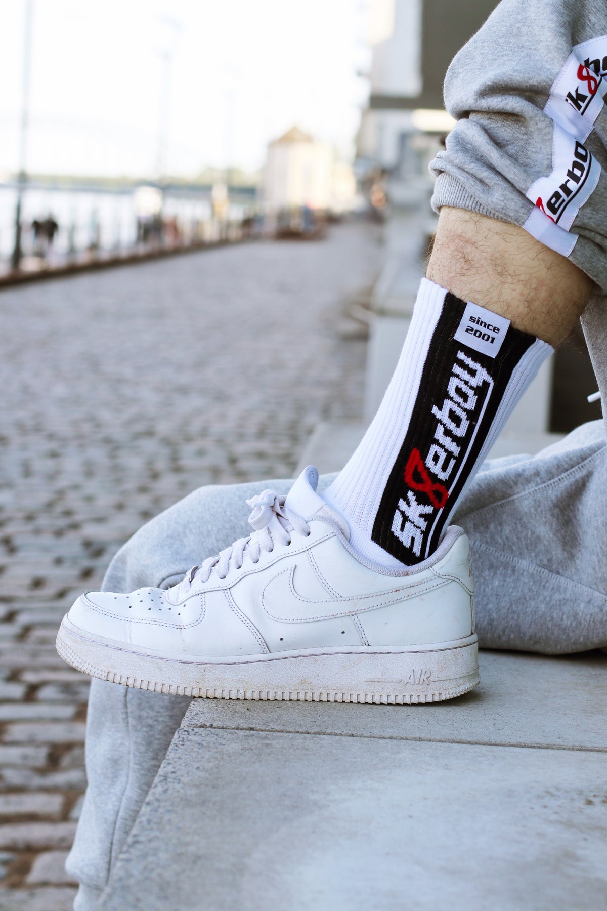 nahaufnahme einer weissen socke von der seite der sk8erboy jubiläums socken 20 jahre smelly socken von einem jungen gay getragen mit dem trainingsanzug in grau von sk8erboy