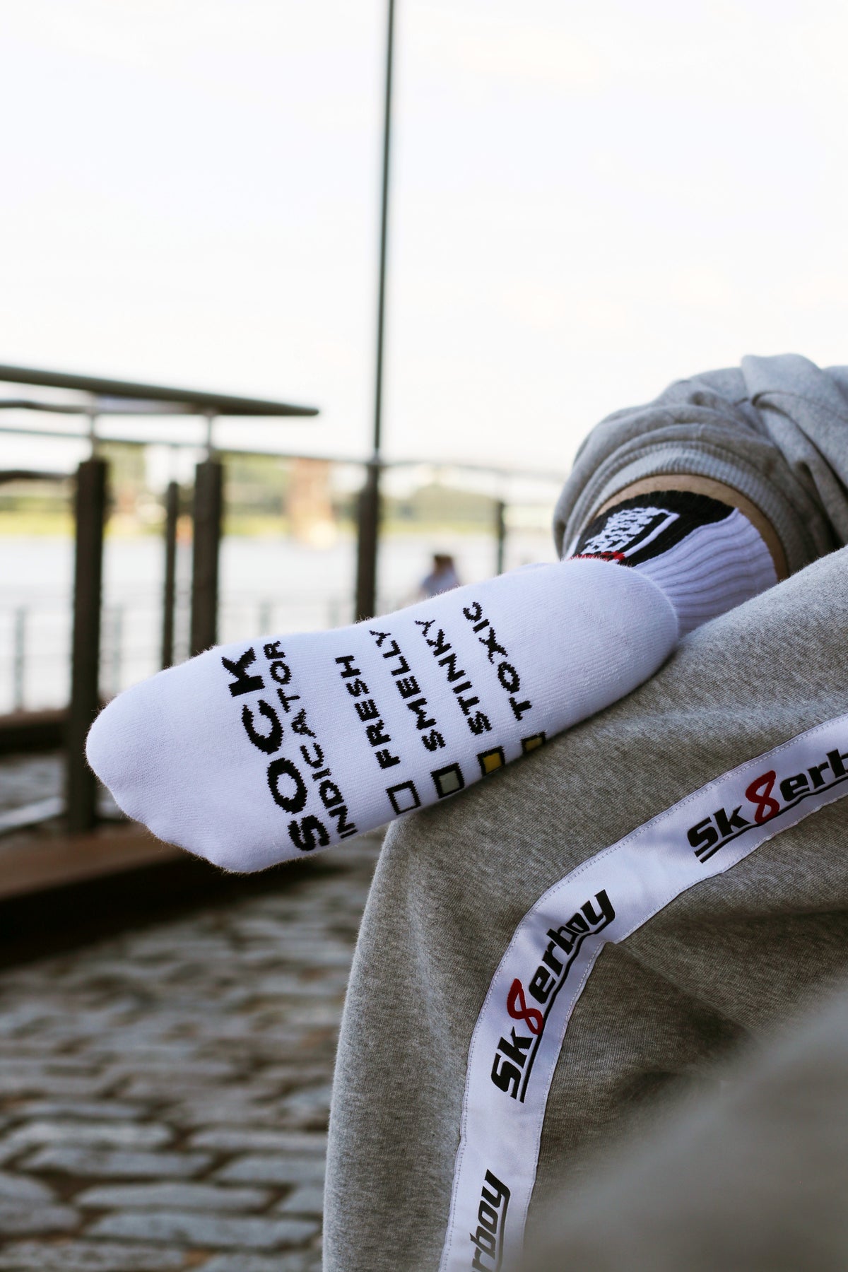 nahaufnahme einer weissen socke von unten der sk8erboy jubiläums socken 20 jahre smelly socken von einem jungen gay getragen mit dem trainingsanzug in grau von sk8erboy