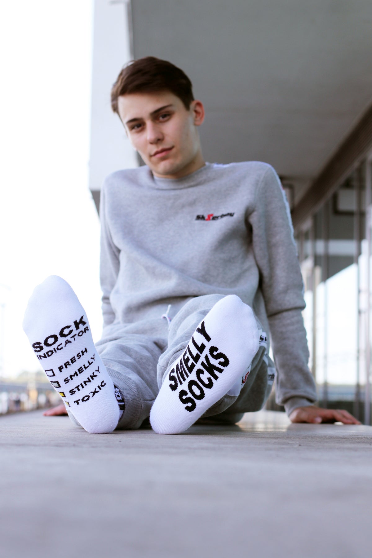 nahaufnahme einer weissen socke von unten der sk8erboy jubiläums socken 20 jahre smelly socken von einem jungen gay getragen mit dem trainingsanzug in grau von sk8erboy