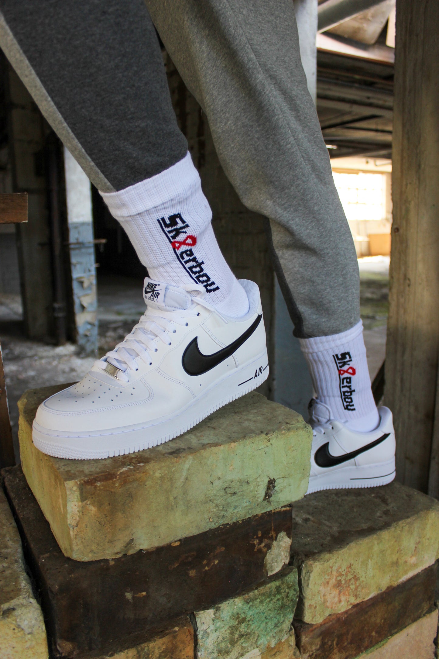 sk8erboy crew socken socks in weiss mit schwarzem schriftzug und roter acht 8 er traegt rot weiss schwarz nike tn tuned 3 drei III er traegt eine graue sweatpant von nike im hintergrund ein lost place farbik