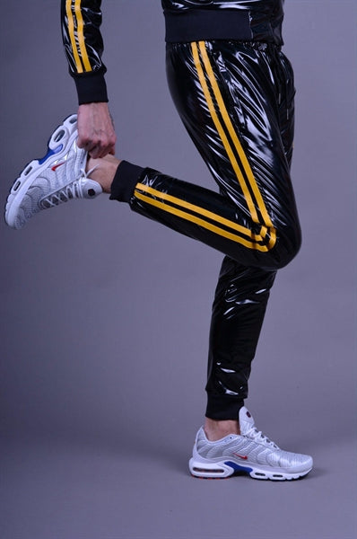 MR Riegillio PVC Tracksuit Hose mit gelben streifen von einem jungen gay getragen in schwarz glänzend mit weissen nike tn sneakern von der seite