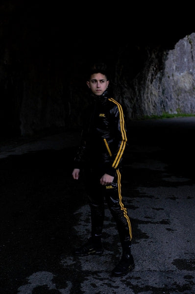 MR Riegillio PVC Tracksuit Hose mit gelben streifen von einem jungen gay getragen in schwarz glänzend mit weissen nike tn sneakern von vorne mit passender jacke