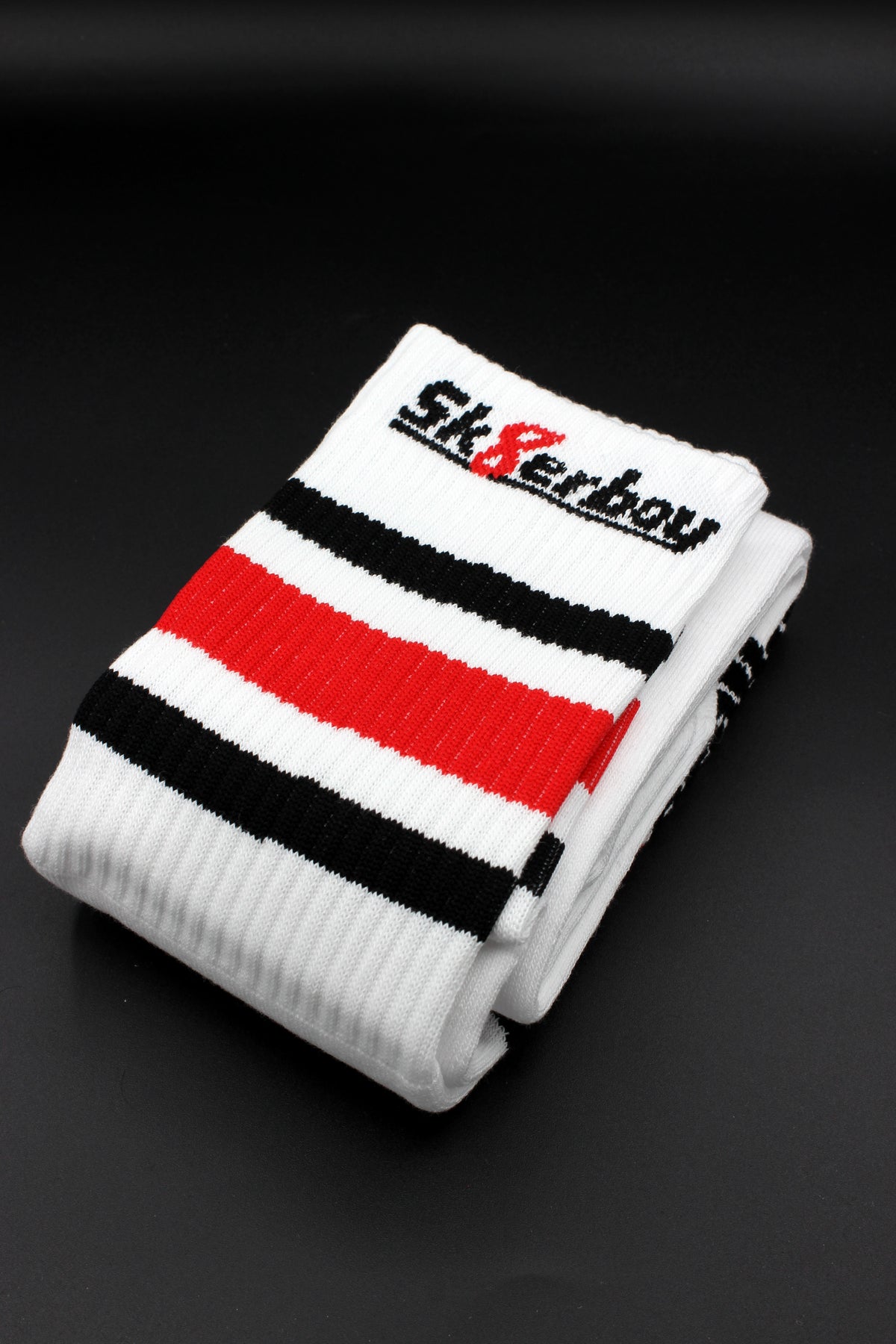 Vue détaillée des chaussettes tube sk8erboy en taille unique, avec bande noire, blanche et rouge à la bordure et grand logo