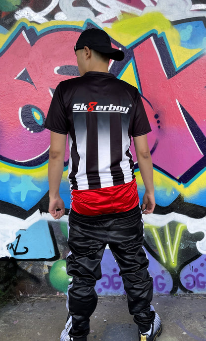 Rückansicht des Sk8erboy® Tikots mit großem Logo, getragen von einem Model in Hocke vor stylischer Graffiti-Kulisse.