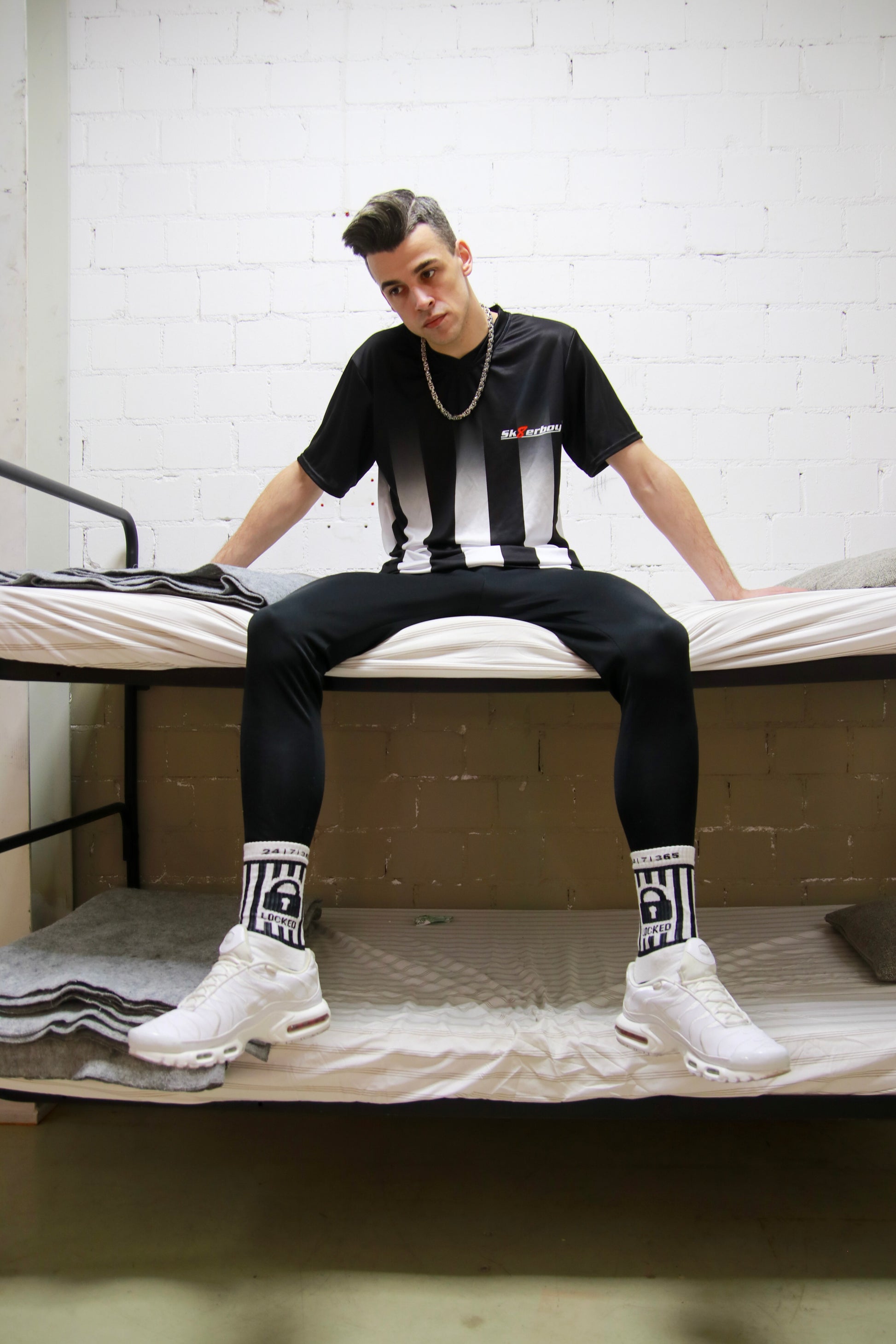 Urbaner Look: Model sitzt mit dem Sk8erboy® Tikot und glänzender Jogginghose in einem Stockbett in einer Gefängniszelle