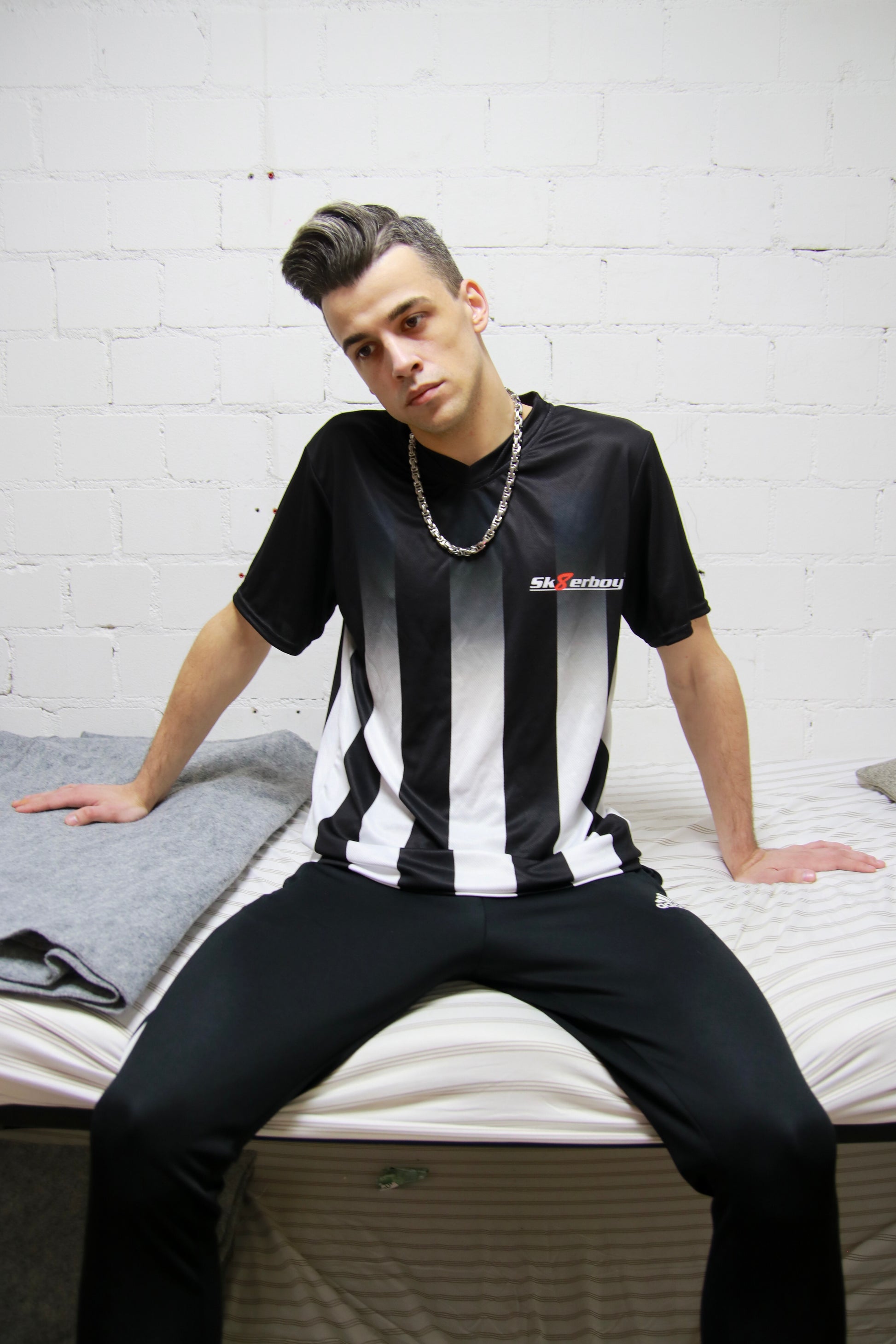 Urbaner Look: Model sitzt mit dem Sk8erboy® Tikot und glänzender Jogginghose in einem Stockbett in einer Gefängniszelle