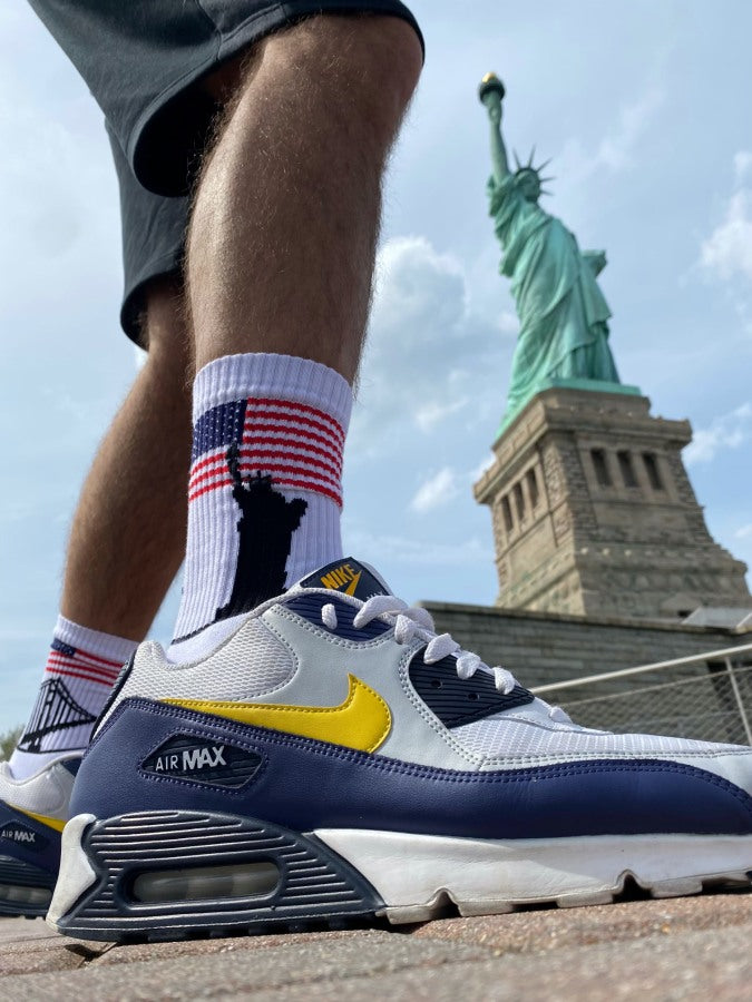 USA flagge auf weissen socken und umriss der golden gate bridge sowie liberty  auf dem linken und rechten socken vor der freiheitsstatue in new york von einem sportlichen jungen getragen mit nike airmax turnschuhen bei sonnenschein