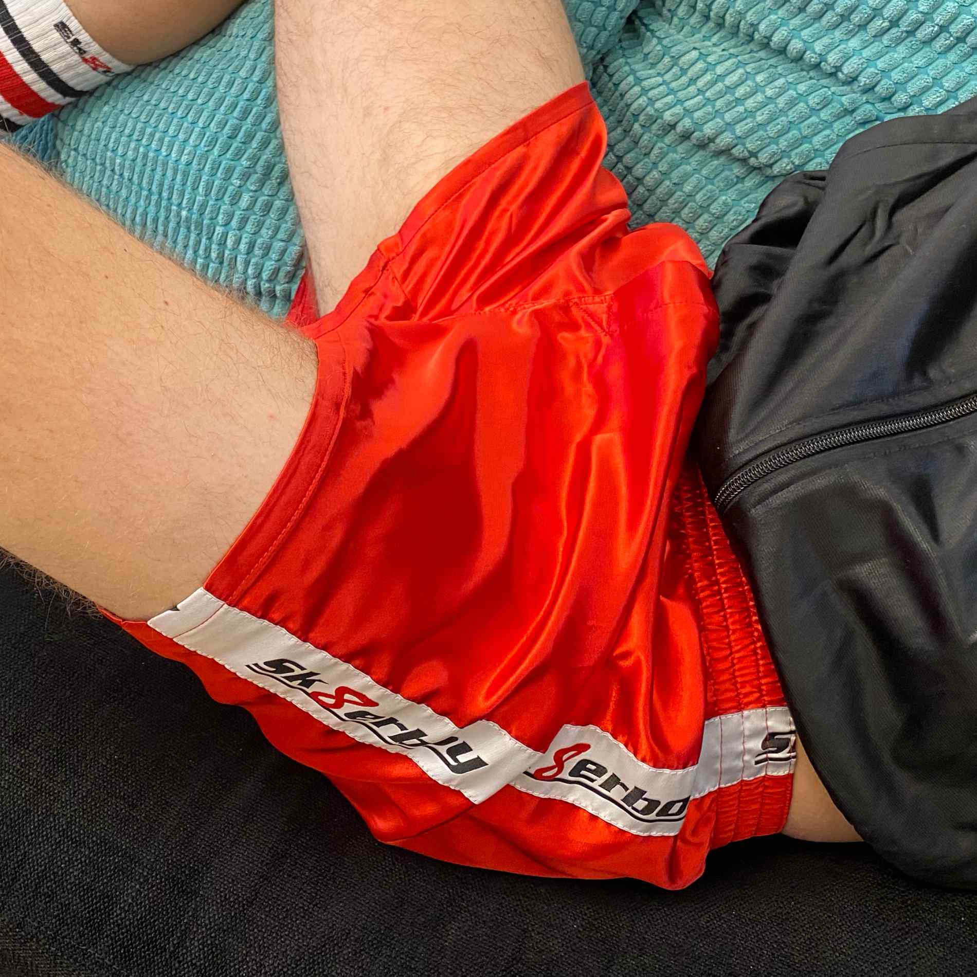 junge auf dem sofa traegt eine feuer rote glanz unterhose in shiny red von sk8erboy mit eingriff und logo seitlich dazu tube socks von sk8erboy und shiny jacket trainingsjacke