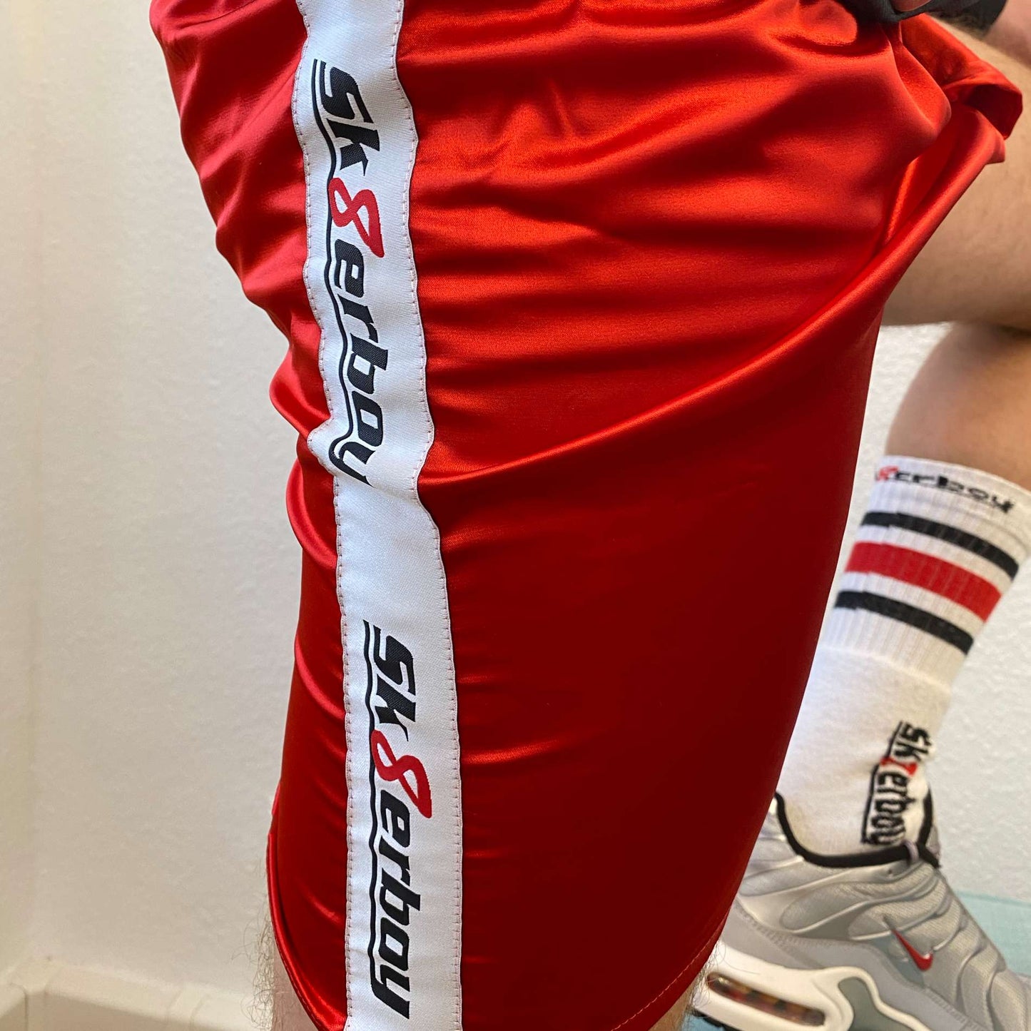 seitliche ansicht einer roten glanz unterhose shiny boxershort von sk8erboy in feuerrot mit logo seitlich und tube socks mit nike tn sneaker in silver