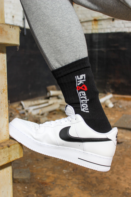 sk8erboy crew socken socks in schwarz black mit weissem sk8erboy schriftzug und roter 8 acht junge traegt weisse nike air force one low afo mit schwarzem swoosh haken im hintergrund ein lost place fabrik