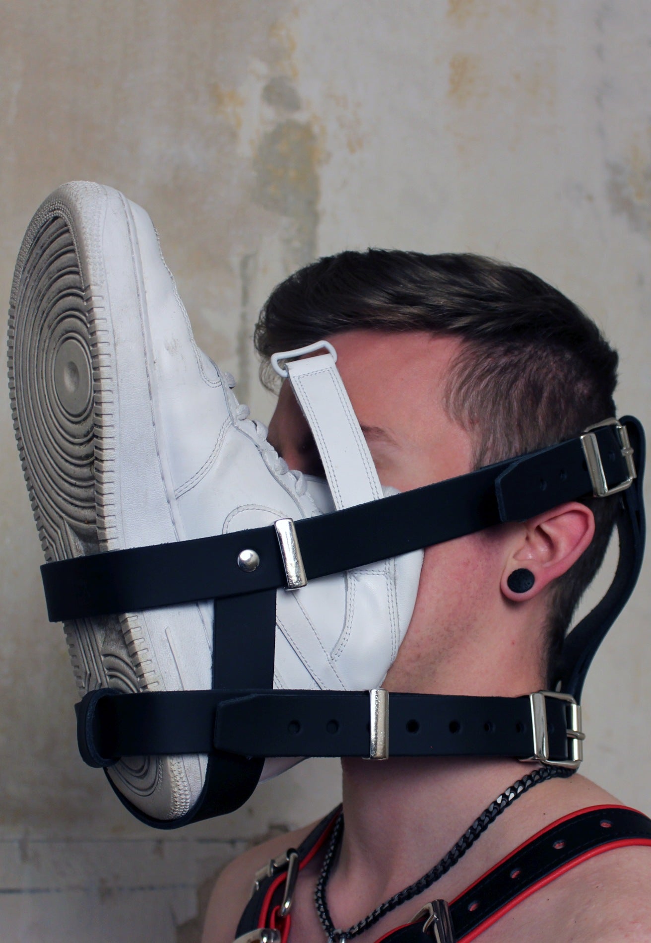 junger gay mit nackten oberkoerper traegt ein gesichts- harness um den kopf mit einem sneaker daran befestigt zum sniffen exklusiv von mister b leder bdsm bei sk8erboy