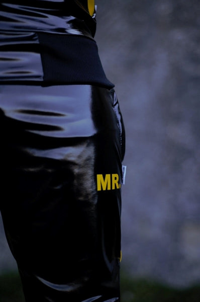 MR Riegillio PVC Tracksuit Hose mit gelben streifen von einem jungen gay getragen in schwarz glänzend mit weissen nike tn sneakern von hinten in nahaufnahme