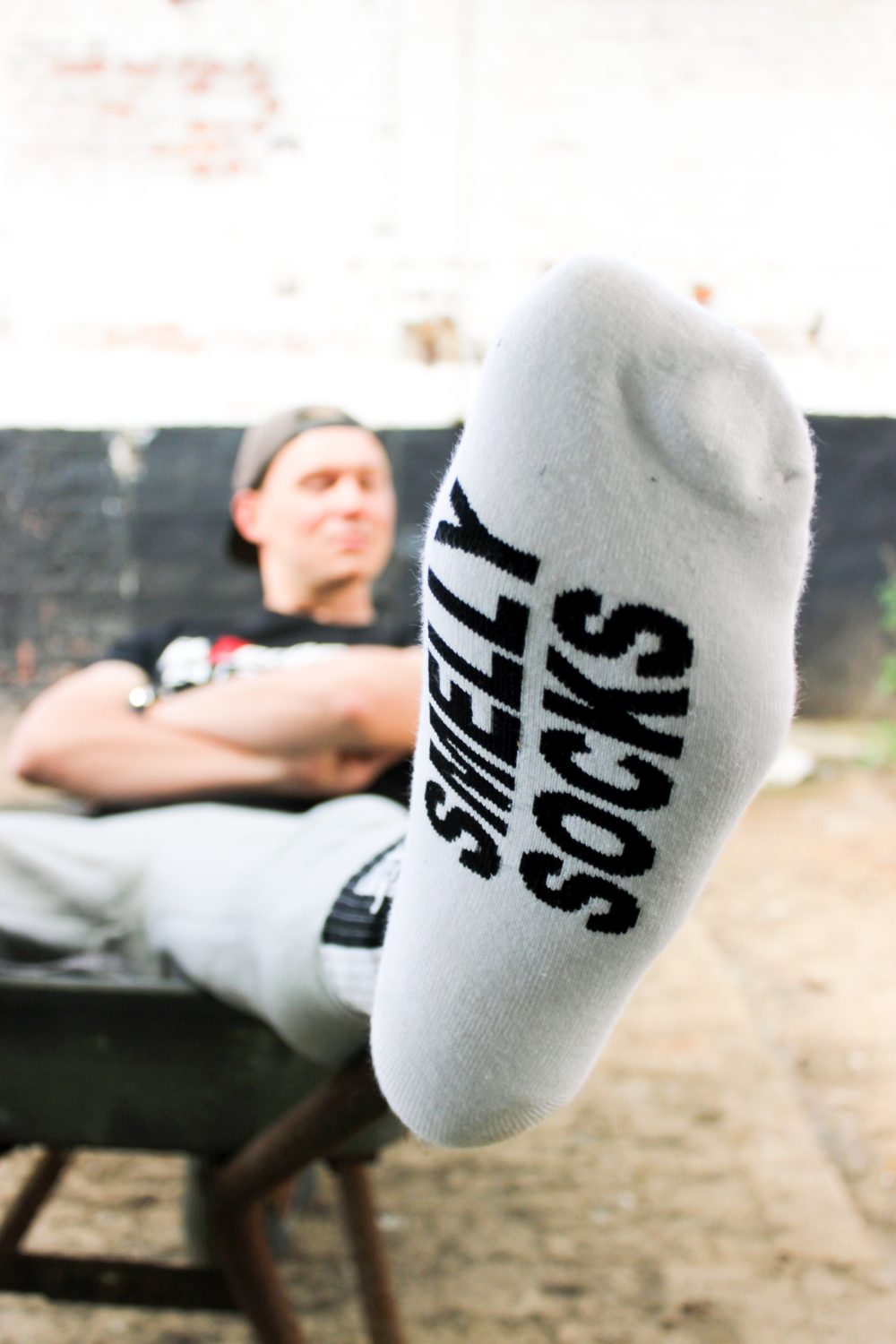 nahaufnahme einer weissen socke von unten der sk8erboy jubiläums socken 20 jahre smelly socken von einem jungen gay getragen der in einer schubkarre sitzt auf einem hof