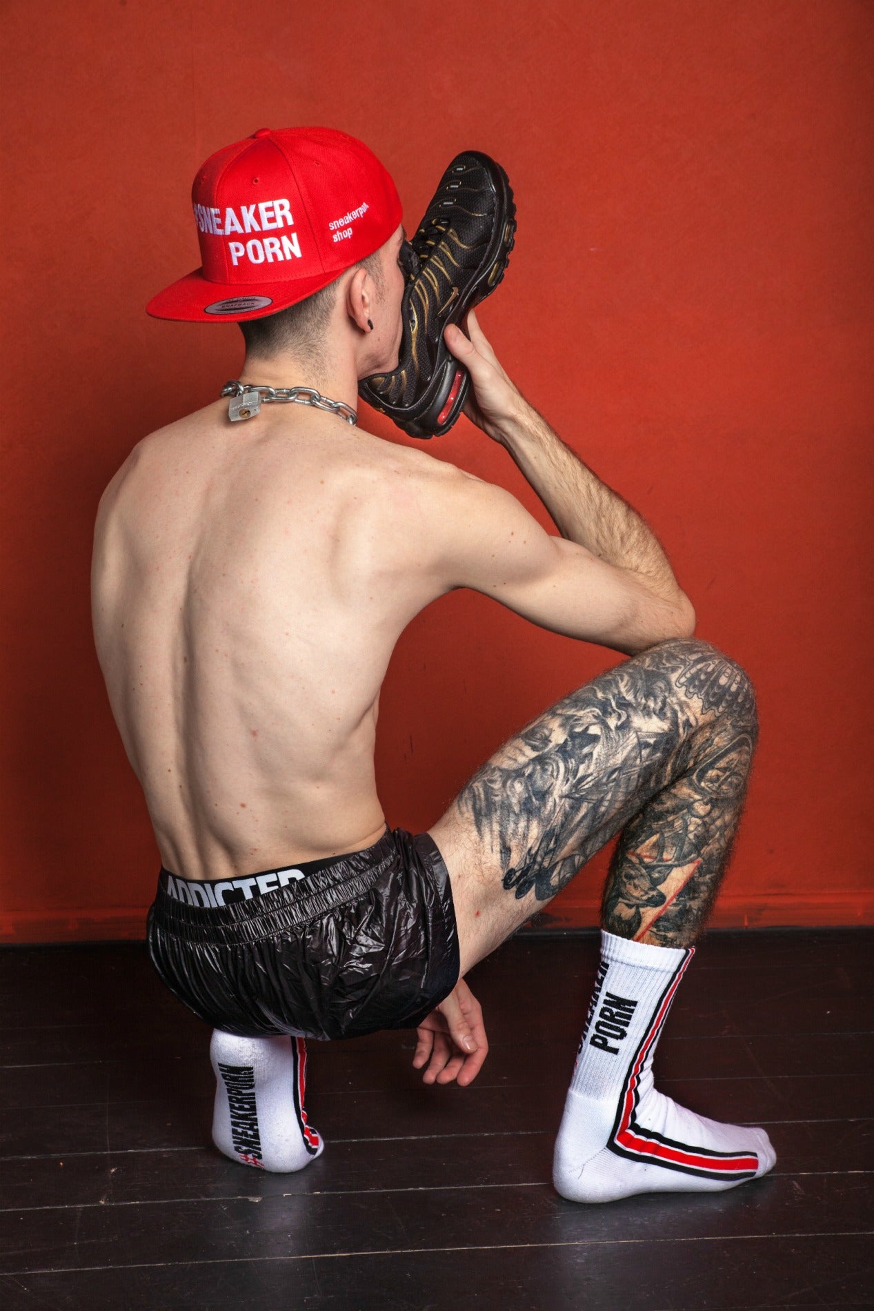 knieender boy mit feiem oberkörper in addicted jock und pvc short mit seinen sneakerporn socken von sk8erboy in weiss und feuerrot