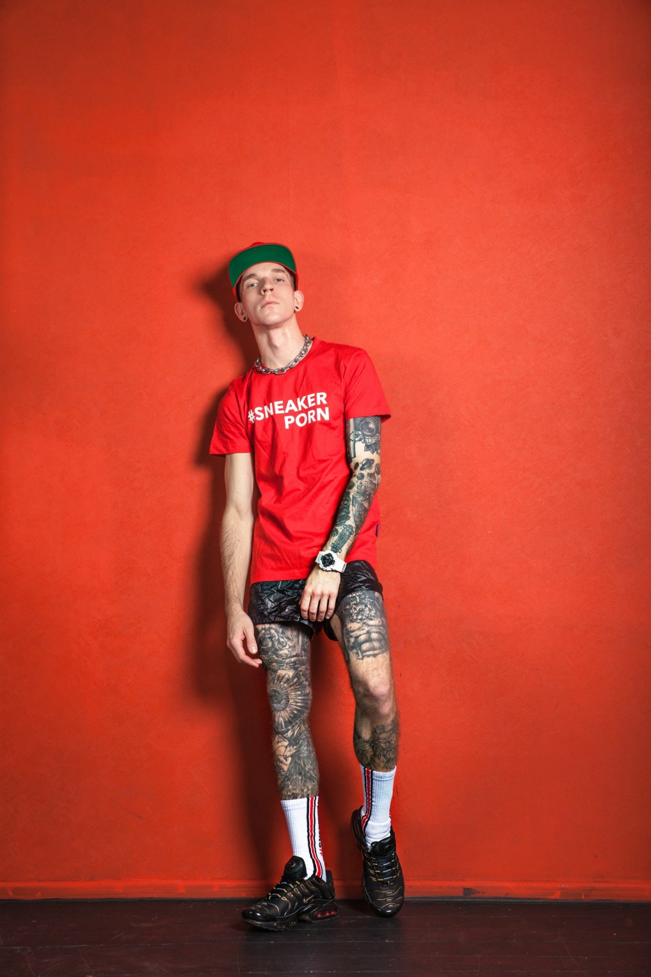 junge mit tattoos in rotem t-shirt und pvc-short trägt nike tn sneaker und sneakerporn socken von sk8erboy in weiss und rot