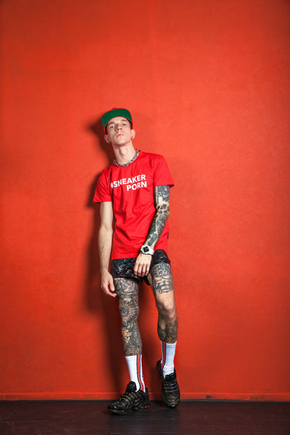 junge mit tattoos in rotem t-shirt und pvc-short trägt nike tn sneaker und sneakerporn socken von sk8erboy in weiss und rot