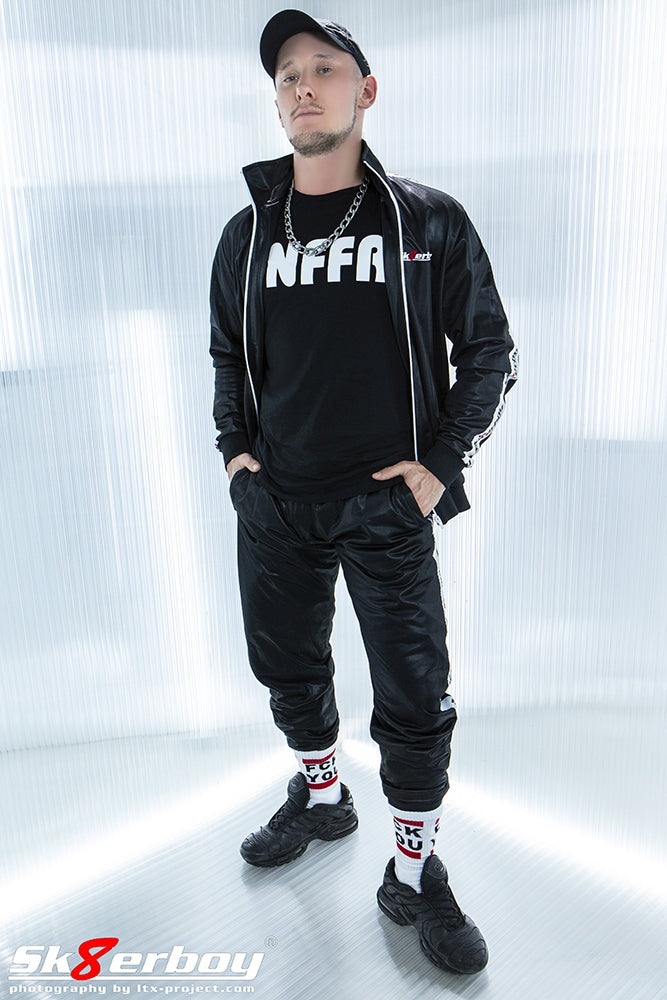 junger gay mit shiny Tracksuits in schwarz von sk8erboy und snffr t-shirt mit fck you socken und nike tn sneaker