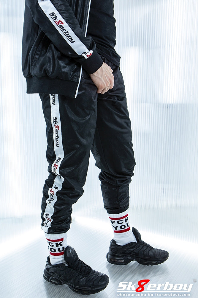 junge mit schwarzer shiny pants von sk8erboy glanz hose und passender jacke dazu fck you socks von sk8erboy und nike-tn sneaks