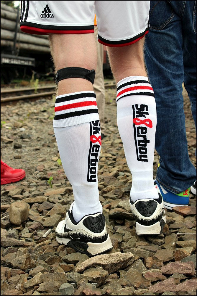 schwarz weiss rote fussball stutzen von sk8erboy mit sneaker auf einem kiesplatz getragen von einem jungen gay mit adidas sport short