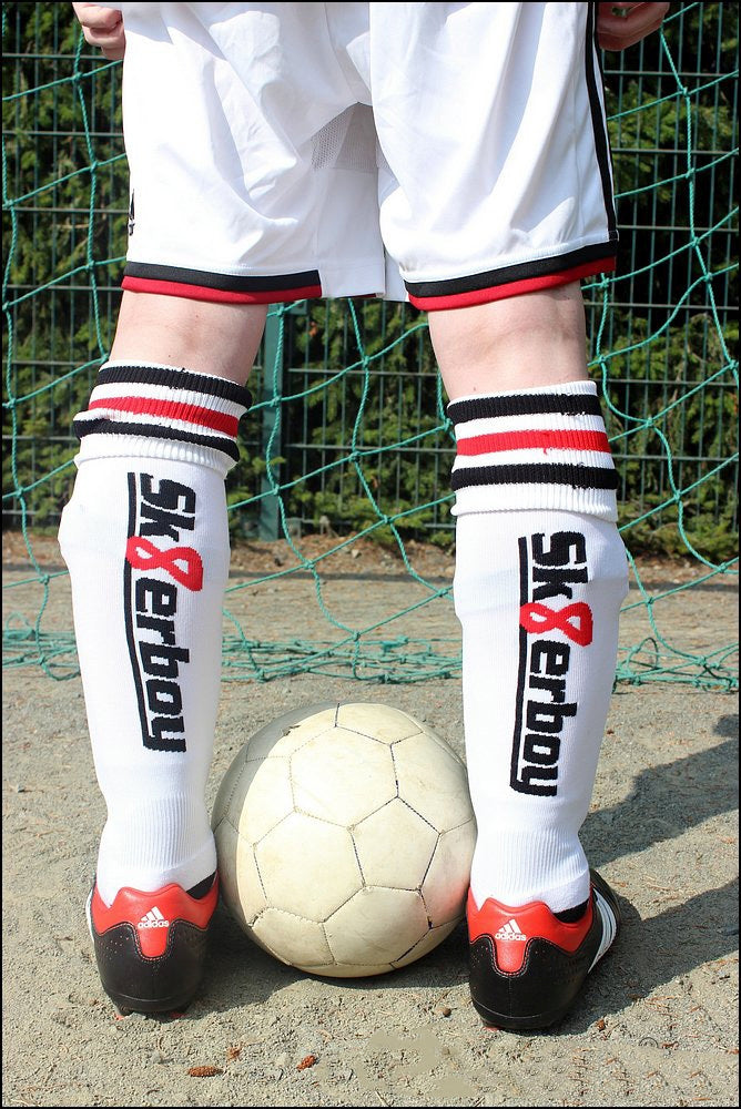 sk8erboy stutzen soccer socks von hinten mit großem logo im tor eines fussballfeldes mit fussballschuhen und fussball in weiss zwischen den beinen des jungen gays