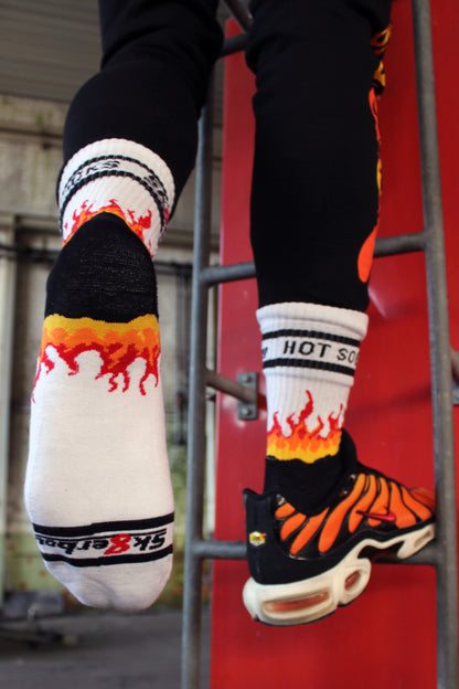 sk8erboy hot socks weisse socken mit schwarzem Schriftzug HOT SOCKS in grossen Buchstaben mit einer schwarzen Linie strich oben und unten ansonsten haben die socken ein flammen muster am Schaft und im fussbereich die flammen sind rot orange und gelb mit einer schwarzen Absetzung der boy Kerl traegt tiger nike tn tuned mit einem roten swosh haken er steht auf einer Leiter die an einem Feuerwehr auto steht