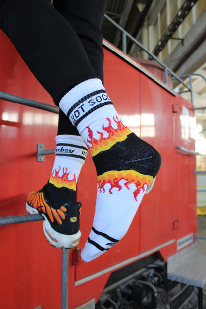 sk8erboy hot socks weisse socken mit schwarzem Schriftzug HOT SOCKS in grossen Buchstaben mit einer schwarzen Linie strich oben und unten ansonsten haben die socken ein flammen muster am Schaft und im fussbereich die flammen sind rot orange und gelb mit einer schwarzen Absetzung der boy Kerl traegt tiger nike tn tuned mit einem roten swosh haken er steht auf einer Leiter die an einem Feuerwehr auto steht mauer haengt