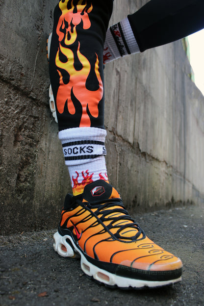 sk8erboy hot socks weisse socken mit schwarzem Schriftzug HOT SOCKS in grossen Buchstaben mit einer schwarzen Linie strich oben und unten ansonsten haben die socken ein flammen muster am Schaft und im fussbereich die flammen sind rot orange und gelb mit einer schwarzen Absetzung der boy Kerl traegt tiger nike tn tuned mit einem roten swosh haken er steht auf einer Leiter die an einem Feuerwehr auto steht mauer haengt