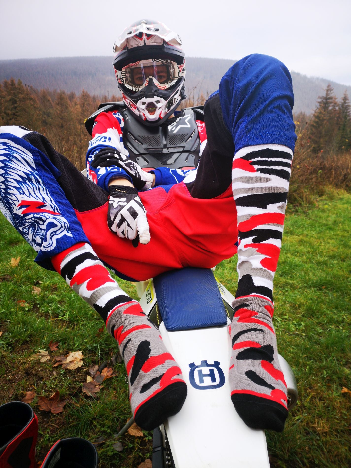 motor cross biker auf seinem motorrad mit helm und den mx socks von sk8erboy in schwarz roten flecktarn muster gegen lederflecken auf socken