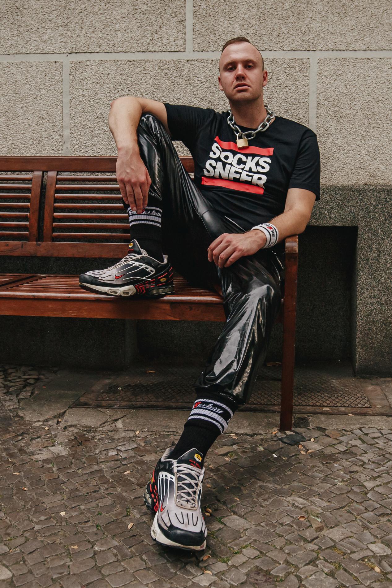 sk8erboy victory socken extra dünn in bekannter qualität jedoch besonders leicht und ideal für den sommer in schwarz von einem jungen gay getragen mit nike tn sneaker und pvc fetisch hose auf einer bank sitzend