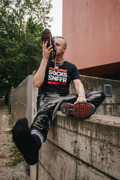 sk8erboy victory socken extra dünn in bekannter qualität jedoch besonders leicht und ideal für den sommer in schwarz von einem jungen gay getragen der an seinen nike tn sneakern snifft und mit pvc hose auf einer mauer sitzt