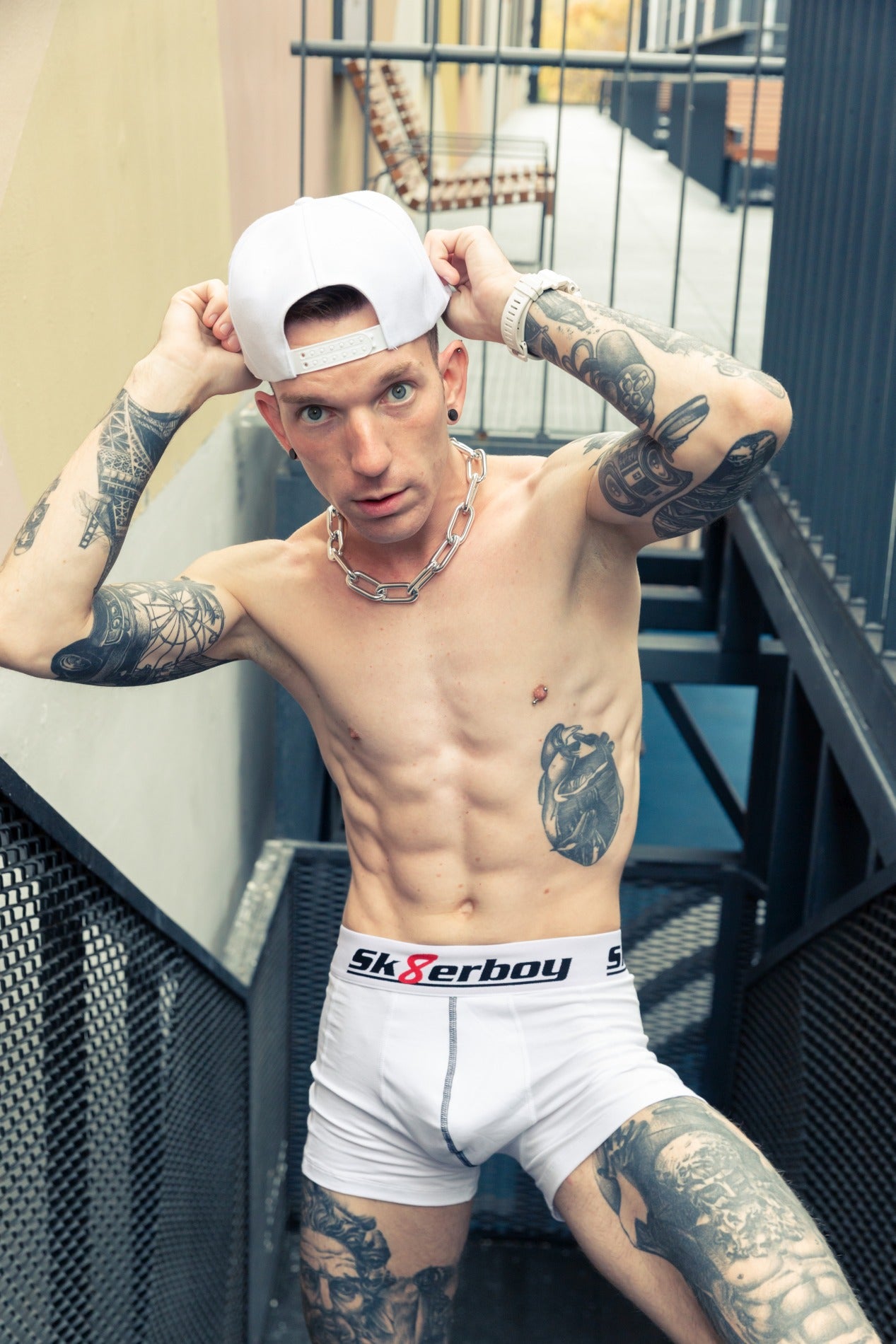 sportlicher oberkörper eines jungen von vorne der eine weisse boxershort von sk8erboy trägt und eine dicke halskette mit kappe auf einer treppe