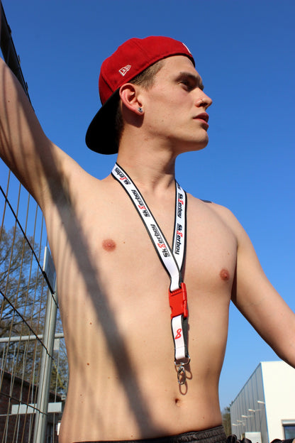 gay mit freiem oberkoerper und roter kappe traegt ein weisses schluesselband von sk8erboy um den hals bei sonnenschein unter blauem himmel